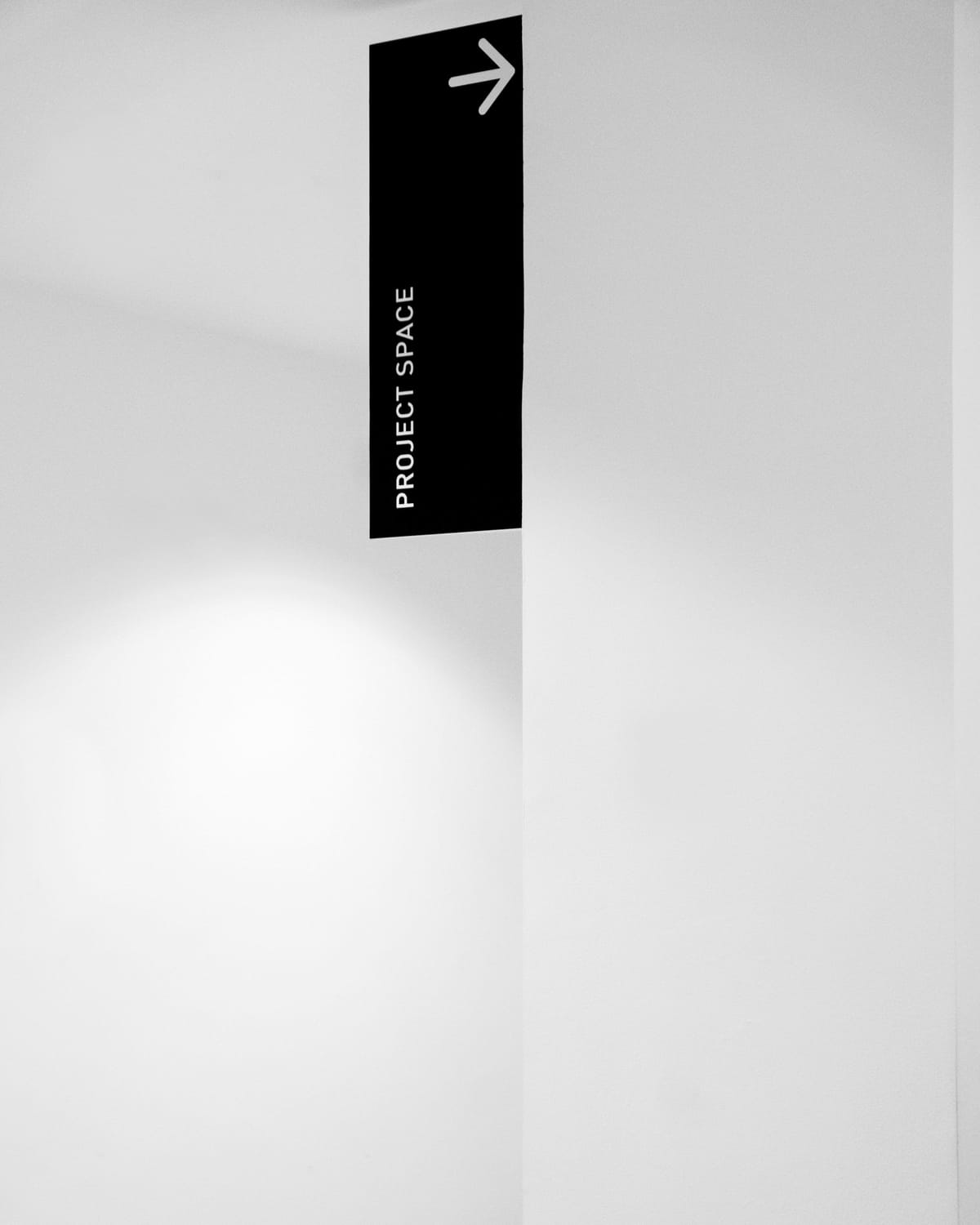 Schwarzes Fahnenschild mit Pfeil und Aufschrift „Project Space“ an einer hellen Wand – minimalistisches Leitsystem